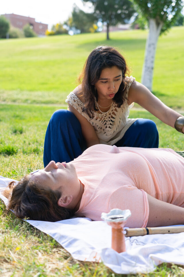 Woman receiving reiki healing session with crystal on chest, lying on blanket in park